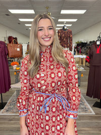 Crimson Charm Dress – A bold crimson midi dress featuring a cream floral-inspired print, feminine ruffle detailing, a flattering tie waist, and pops of blue trim