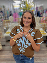 Bluebell bloom embroidered top -  features light blue floral embroidery on the front, matching blue trim along the round neckline and tiered flutter sleeves, and a split neckline