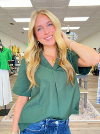 The Scarlett blouse - a rich green blouse featuring a pleated stand collar, short sleeves with stitched cuff details.