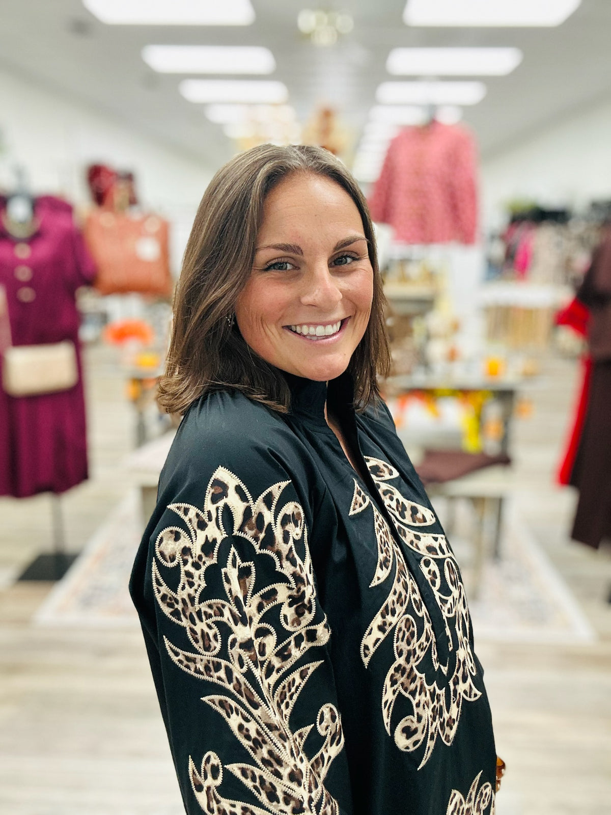 The Savannah Luxe Leopard Embroidered Tunic features a classic black fabric with leopard- inspired embroidered detailing. Ruffled mock neckline and three- quarter puff sleeves.
