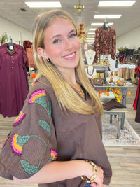 Meadow Muse Top — A rich chocolate-brown textured top featuring colorful floral embroidery, puff sleeves, and a feminine ruffled neckline