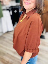 The Harper blouse - Relaxed oversized blouse in a rich rust-brown color, featuring a split V-neck collar, flowy short sleeves, and a scalloped bottom hem