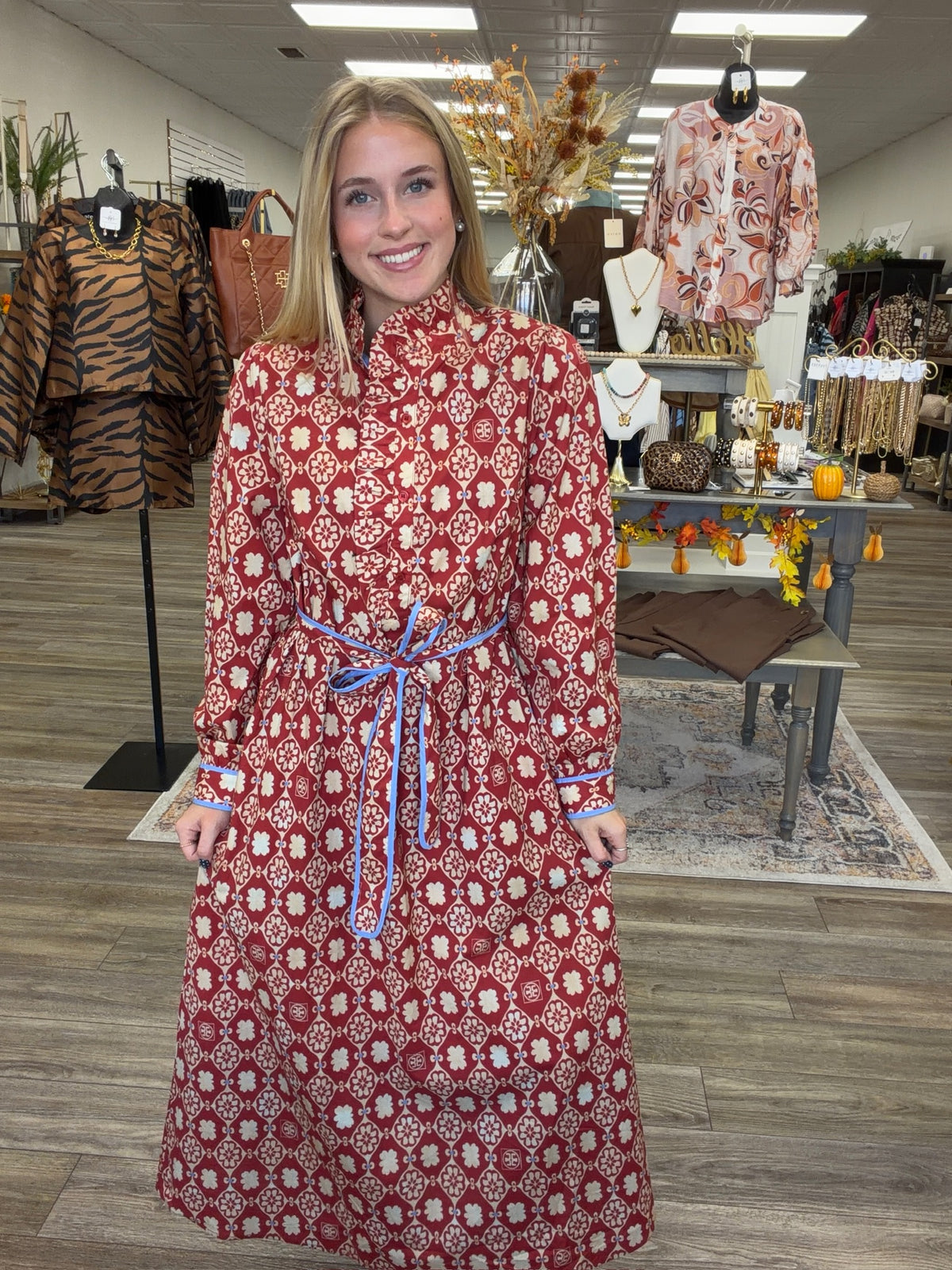Crimson Charm Dress – A bold crimson midi dress featuring a cream floral-inspired print, feminine ruffle detailing, a flattering tie waist, and pops of blue trim