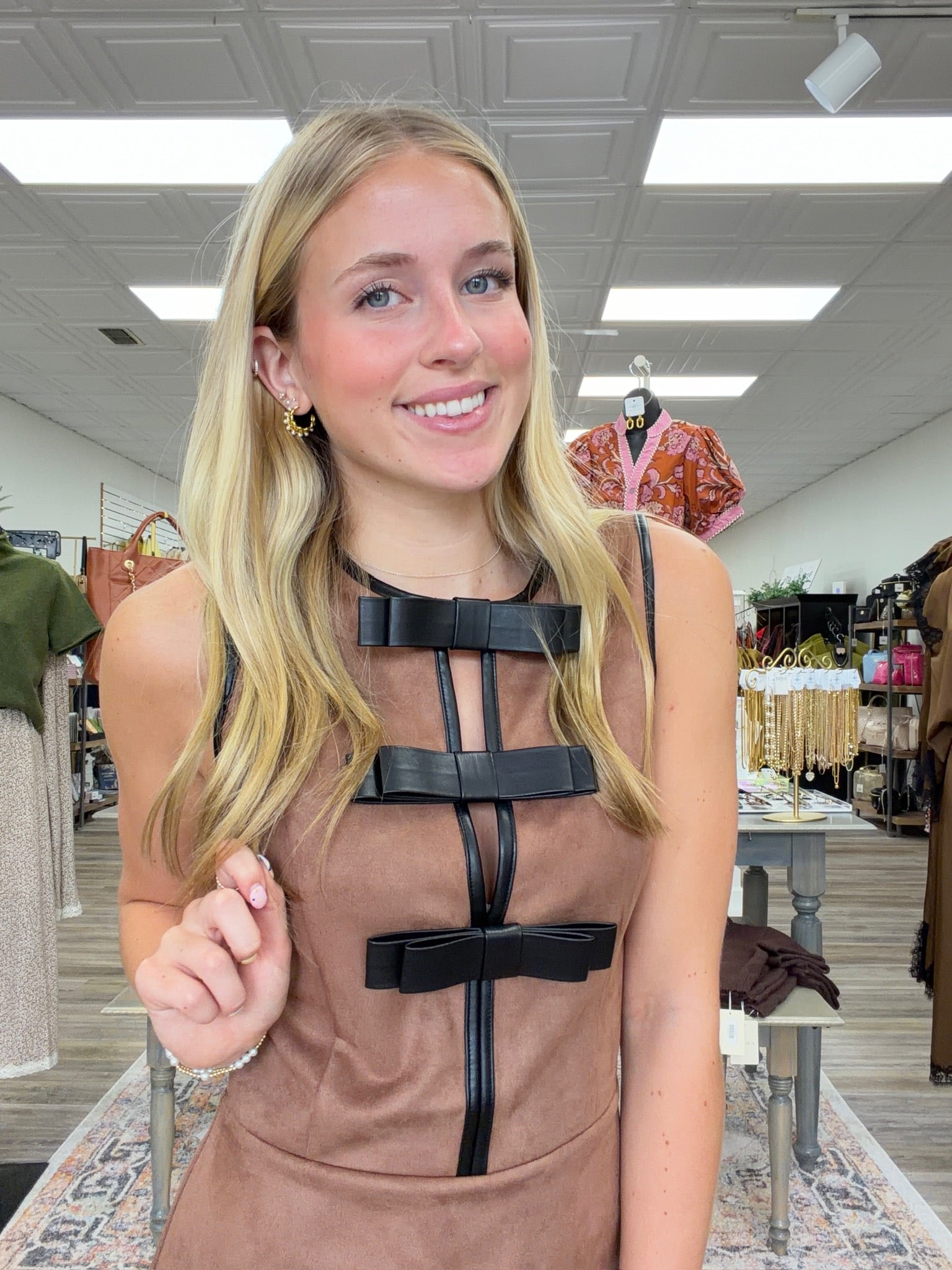 The Caroline Bow Dress - Camel faux-suede mini dress featuring a flattering sleeveless silhouette, contrasting black trim, and statement bow details down the front