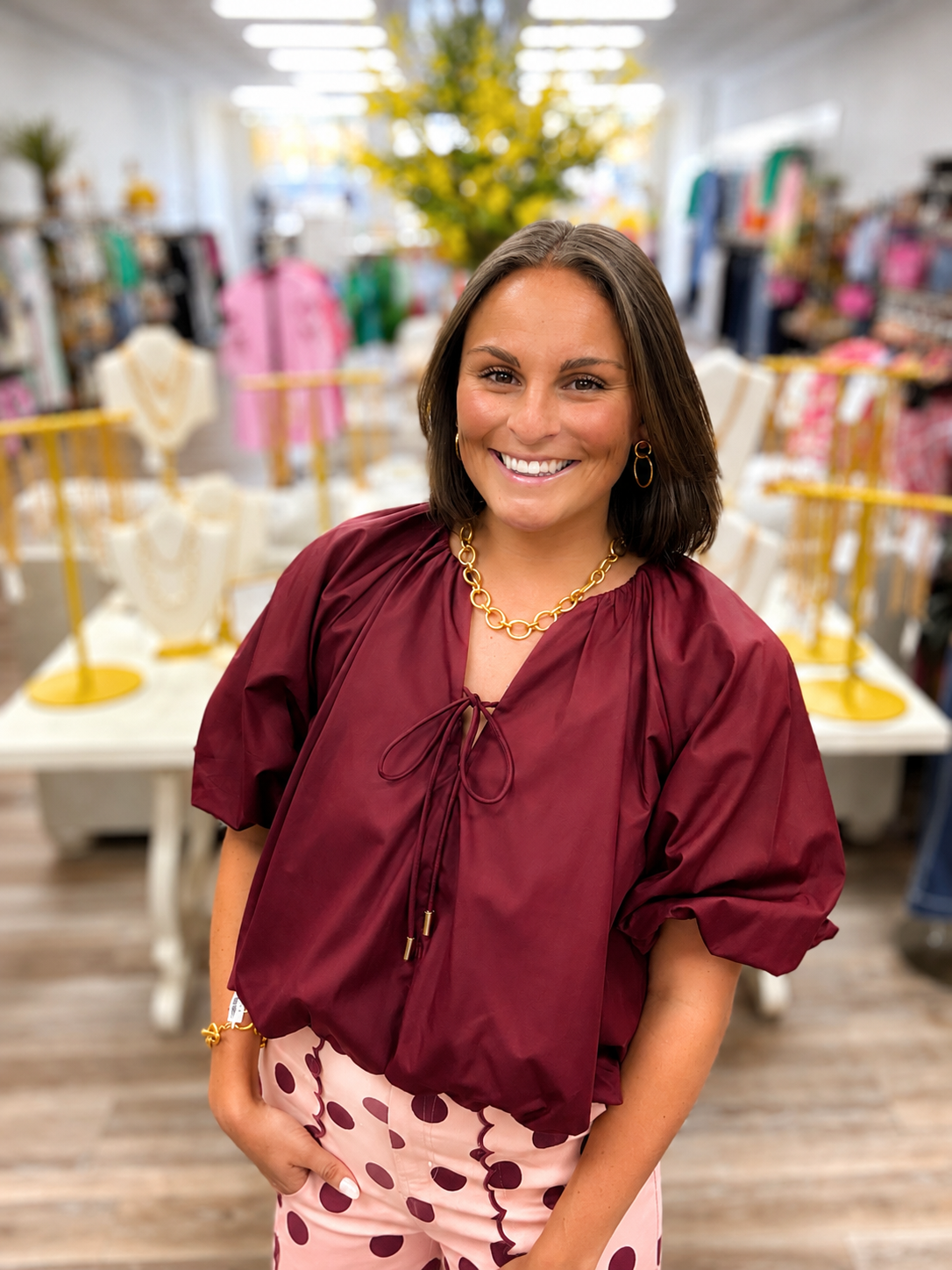 The Jolene blouse - dark berry colored blouse, deep V-neck with front tie, puff sleeves, gathered stretchy hem at the bottom, lightweight and airy fit.