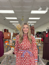 Crimson Charm Dress – A bold crimson midi dress featuring a cream floral-inspired print, feminine ruffle detailing, a flattering tie waist, and pops of blue trim