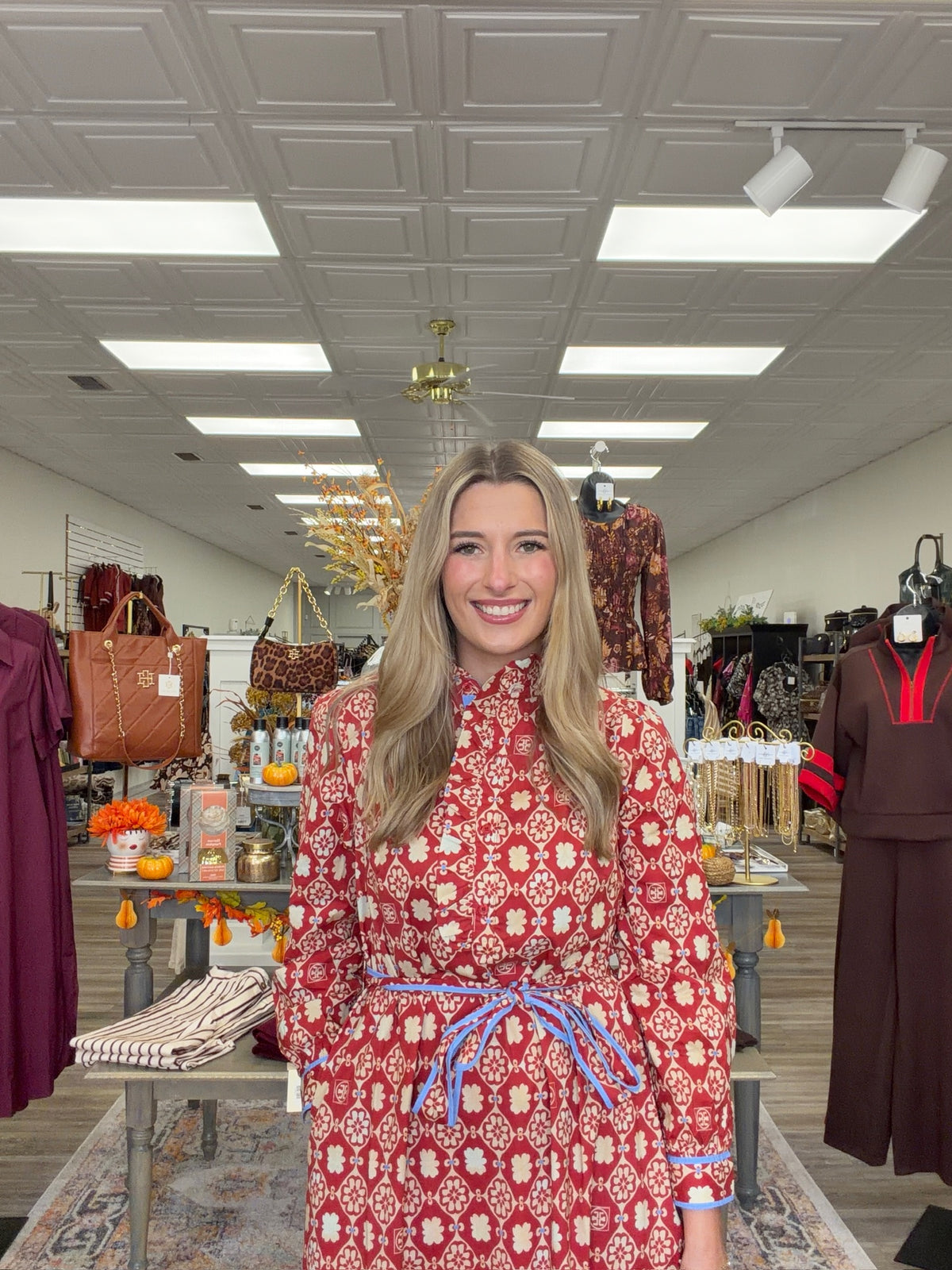 Crimson Charm Dress – A bold crimson midi dress featuring a cream floral-inspired print, feminine ruffle detailing, a flattering tie waist, and pops of blue trim