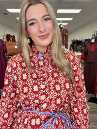 Crimson Charm Dress – A bold crimson midi dress featuring a cream floral-inspired print, feminine ruffle detailing, a flattering tie waist, and pops of blue trim