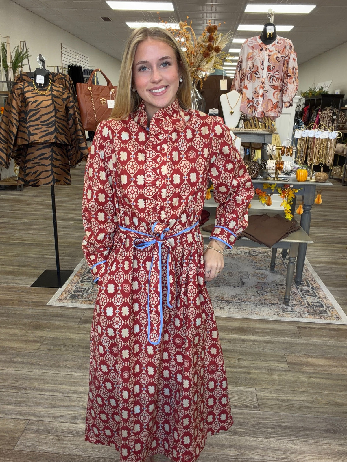 Crimson Charm Dress – A bold crimson midi dress featuring a cream floral-inspired print, feminine ruffle detailing, a flattering tie waist, and pops of blue trim