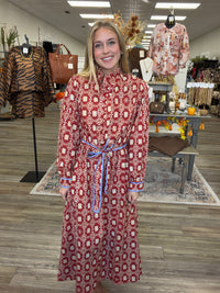 Crimson Charm Dress – A bold crimson midi dress featuring a cream floral-inspired print, feminine ruffle detailing, a flattering tie waist, and pops of blue trim