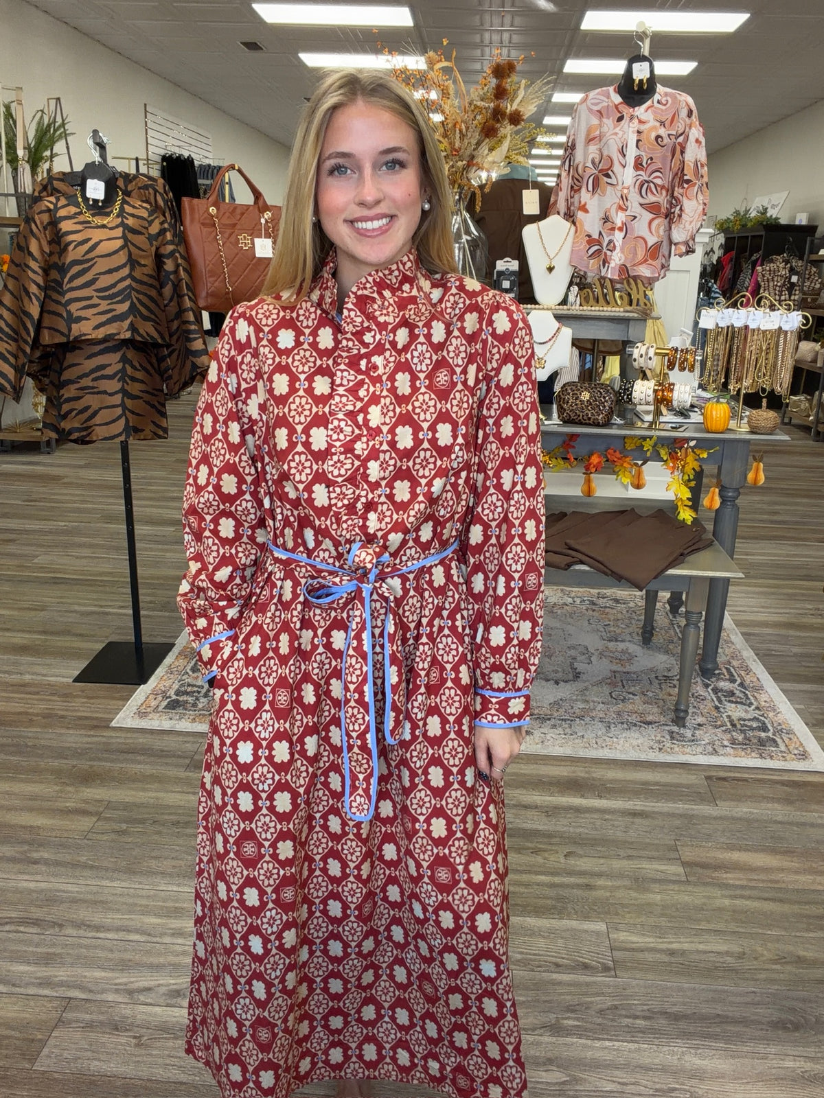 Crimson Charm Dress – A bold crimson midi dress featuring a cream floral-inspired print, feminine ruffle detailing, a flattering tie waist, and pops of blue trim