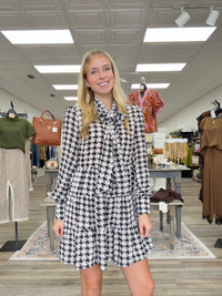 The Blair dress - Black-and-cream houndstooth dress with a tie-neck detail, long sleeves, and a flowy tiered silhouette.
